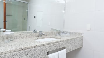 A modern bathroom with a granite countertop, two sinks, a glass shower enclosure, and a large mirror.