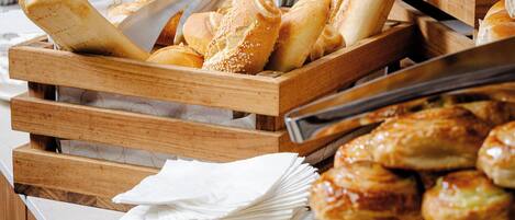 A buffet with various breads and pastries, including baguettes and croissants, arranged on wooden stands.