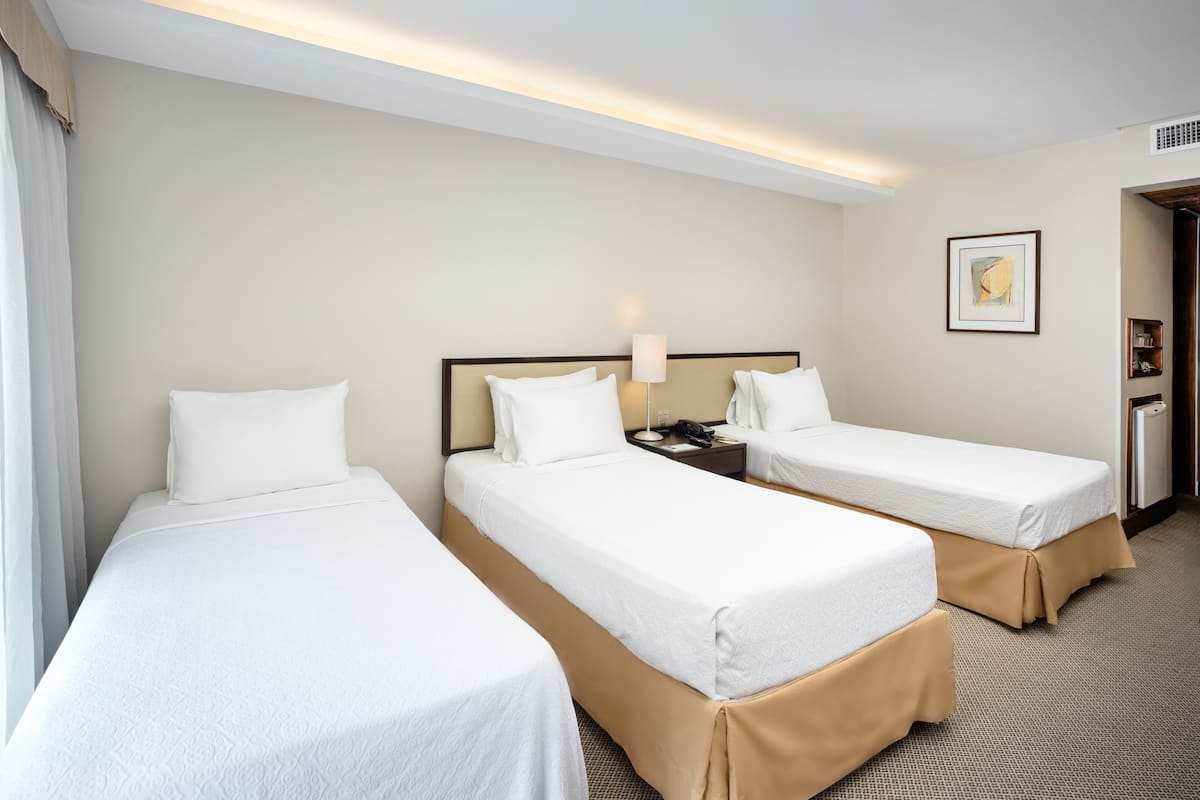 A hotel room with two single beds, a bedside table with a lamp, a framed picture on the wall, and a door leading to a bathroom.