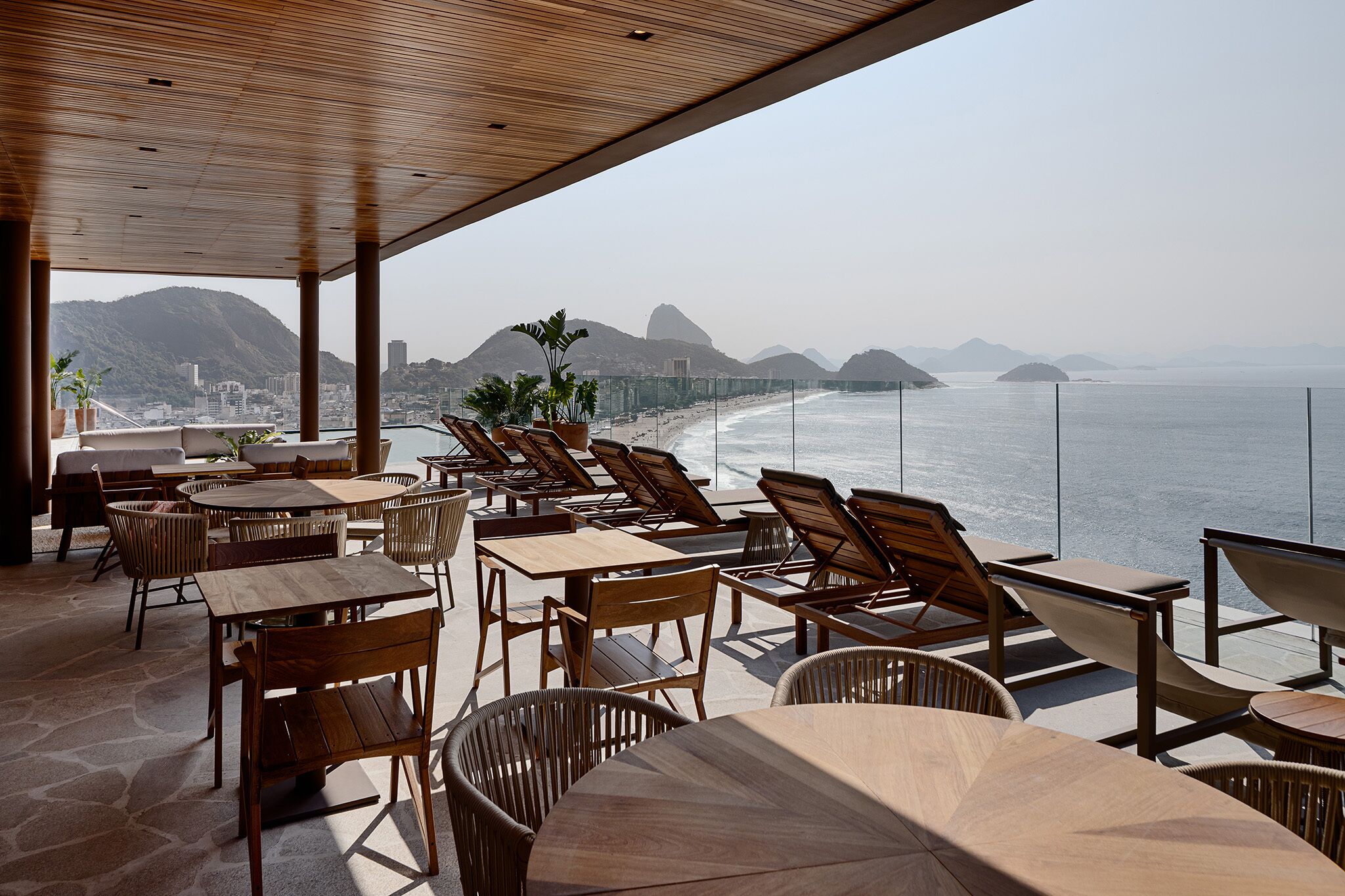 Un espacio al aire libre con mesas y sillas, con vistas a la playa y las montañas.