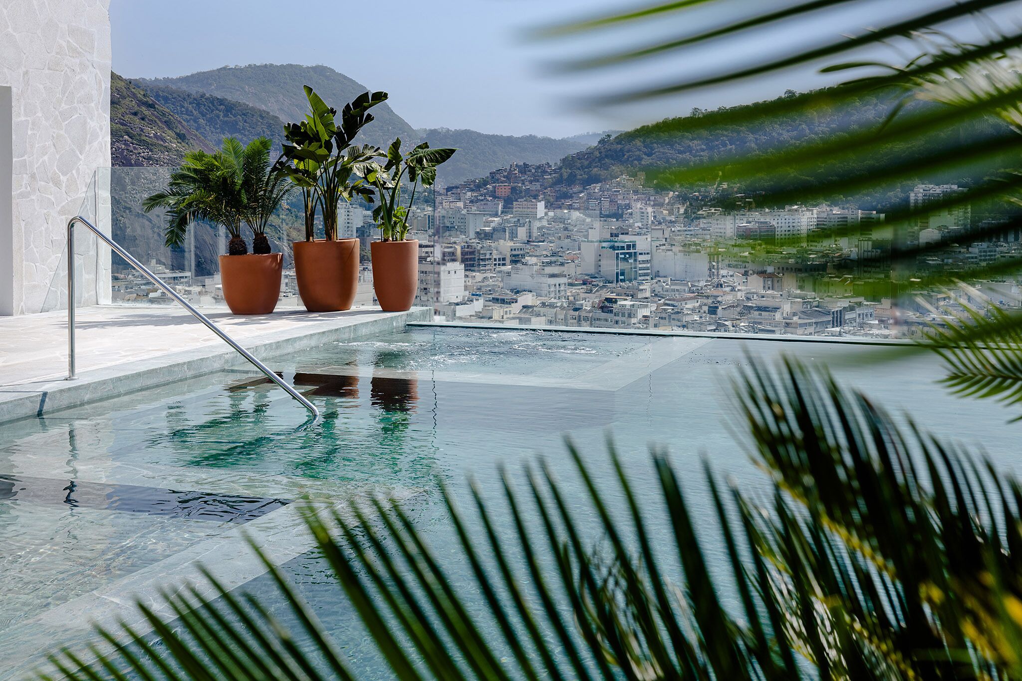 Ein Infinity-Pool mit Blick auf die Stadtlandschaft, Blumentöpfen und einem Metallgeländer.