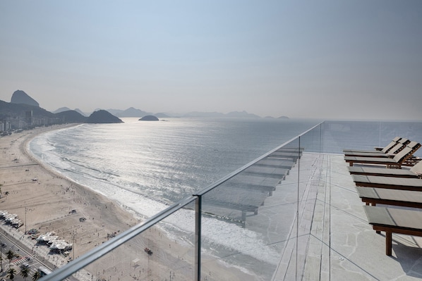 A beachside view from a balcony with sun loungers, a sandy beach, and distant mountains. - Othon Palace Copacabana Rio (Rio de Janeiro)