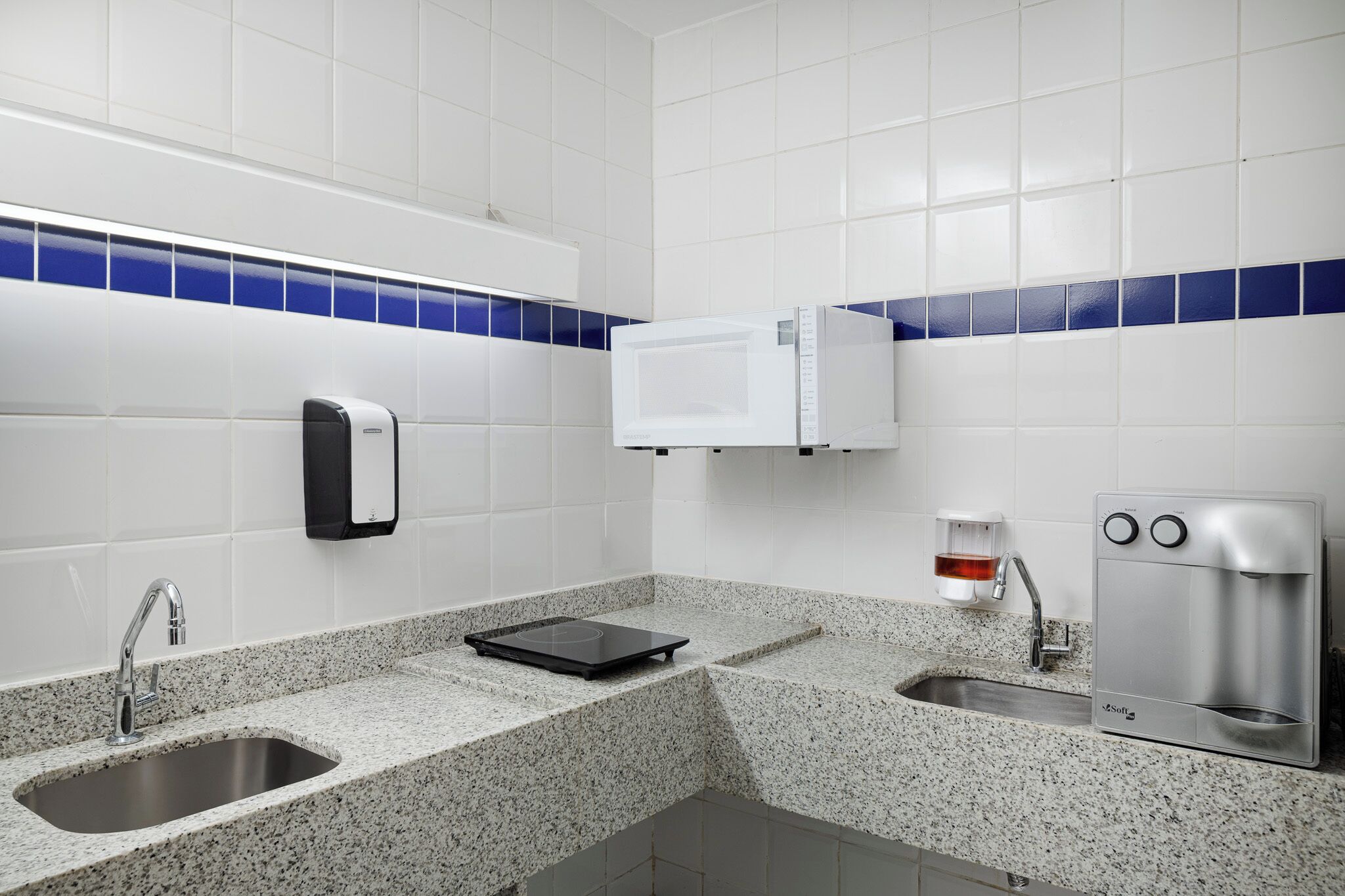 A modern bathroom with a granite countertop, a sink, a soap dispenser, a microwave, and a coffee machine.