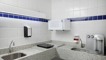A modern bathroom with a granite countertop, a sink, a soap dispenser, a microwave, and a coffee machine.