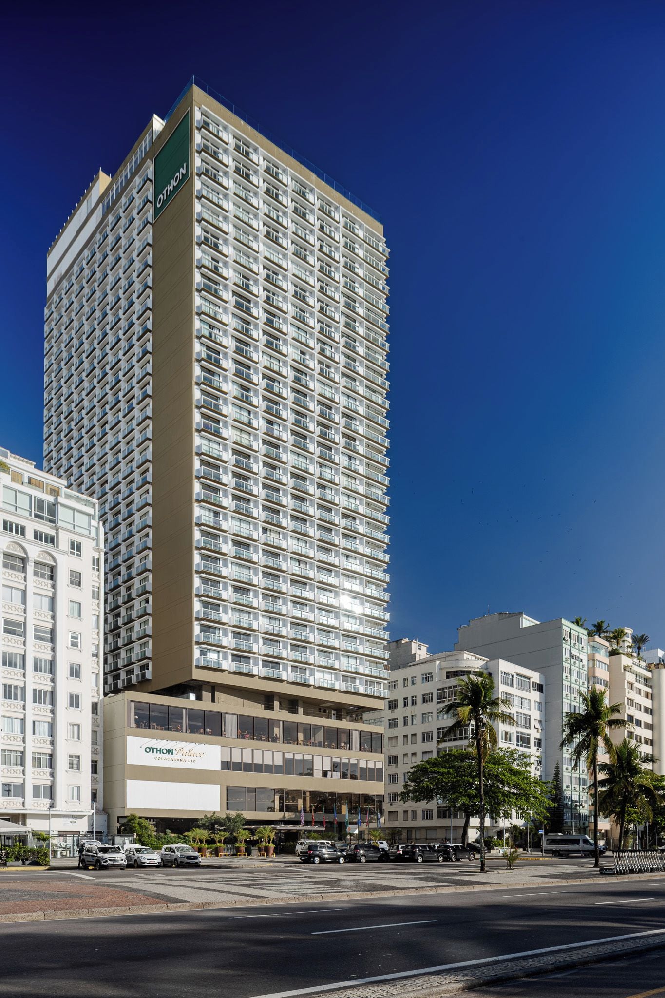 Un hotel de gran altura con varios pisos, un letrero llamativo en la fachada y un área de estacionamiento al frente.