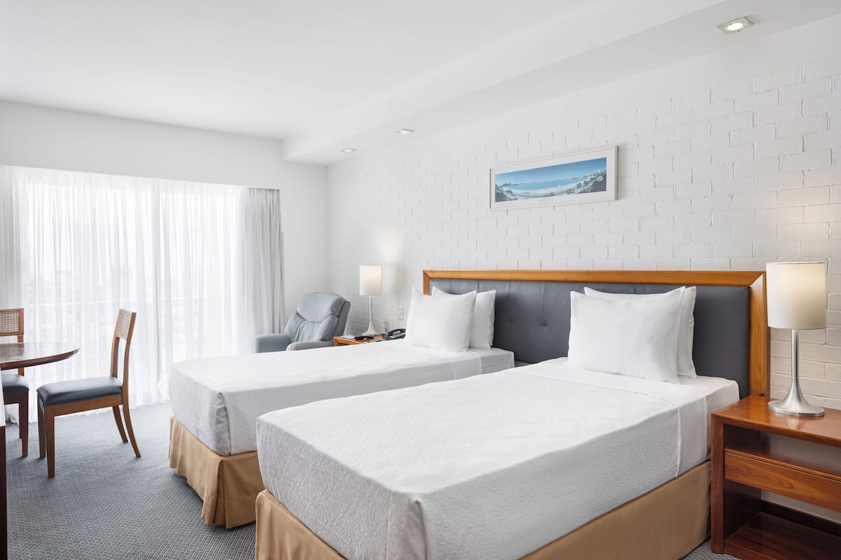 A hotel room with two beds, a desk, a chair, a lamp, and a picture on the wall.