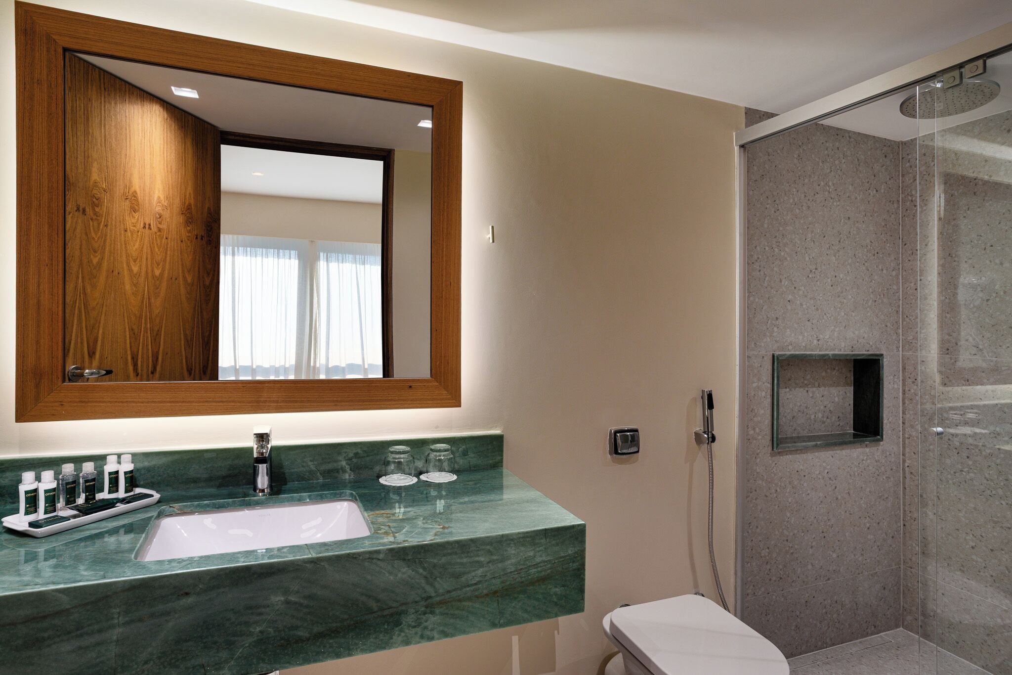 Een badkamer met een marmeren wastafel, een spiegel met houten lijst en een douche met glazen wanden.