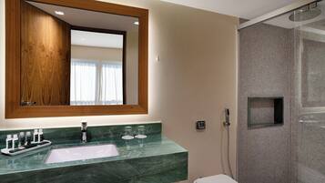 Een badkamer met een marmeren wastafel, een spiegel met houten lijst en een douche met glazen wanden.