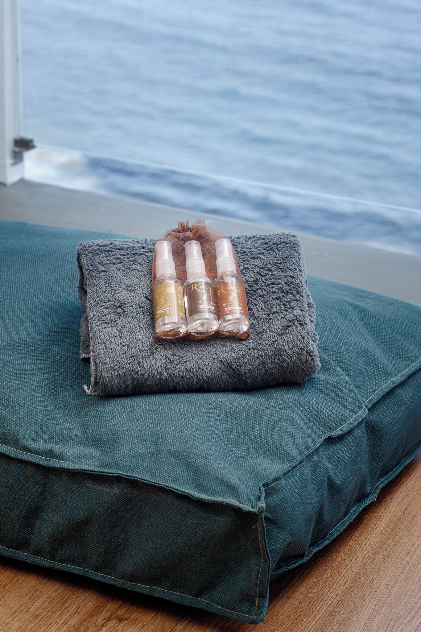 A grey towel with three bottles on a teal pillow.