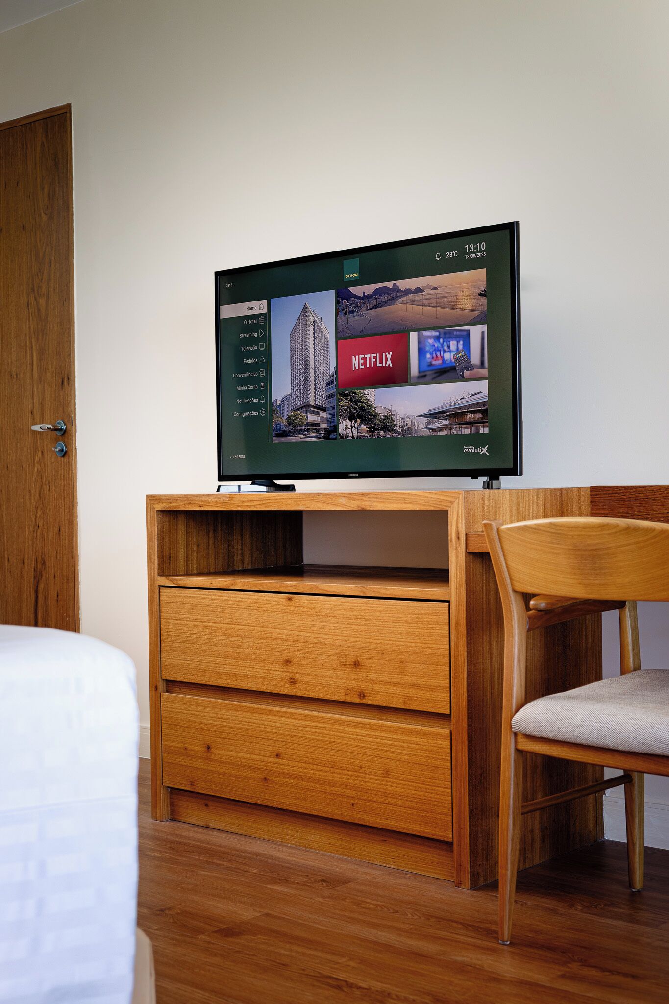 A television mounted on a wooden cabinet with a wooden chair beside it.