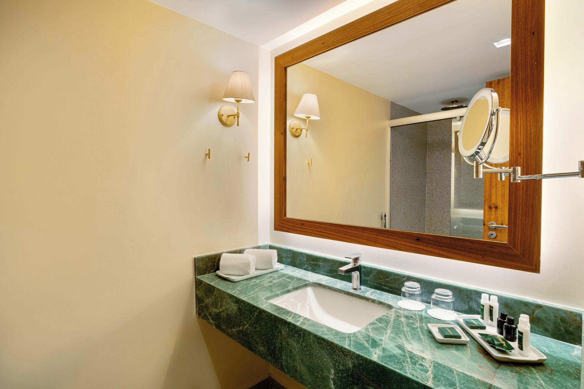 A bathroom with a marble sink, two wall-mounted lamps, a large mirror, and toiletries on the counter.