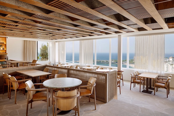 A modern restaurant with high ceilings, wooden beams, and large windows offering a view of the ocean. - Othon Palace Copacabana Rio (Rio de Janeiro)