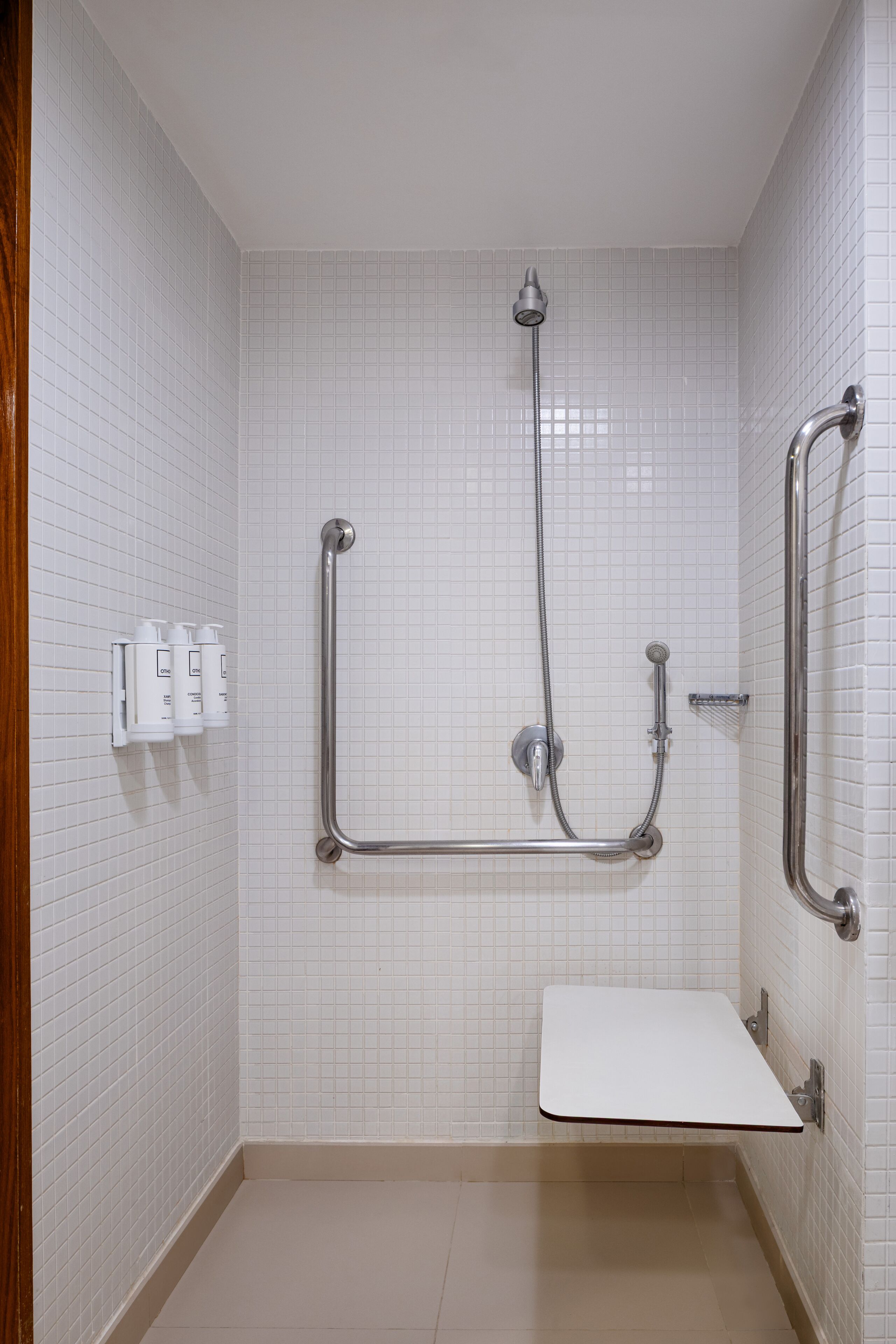 A bathroom with white tiled walls, a white sink, and a shower with grab bars.