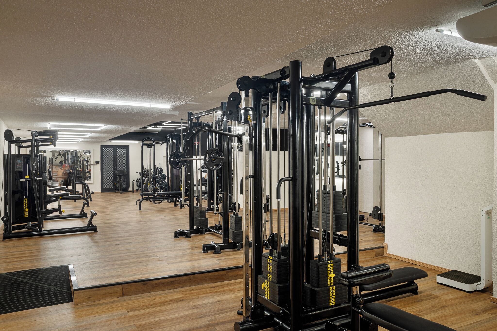 Uma academia com diversos equipamentos de exercícios, piso de madeira e um espelho na parede.