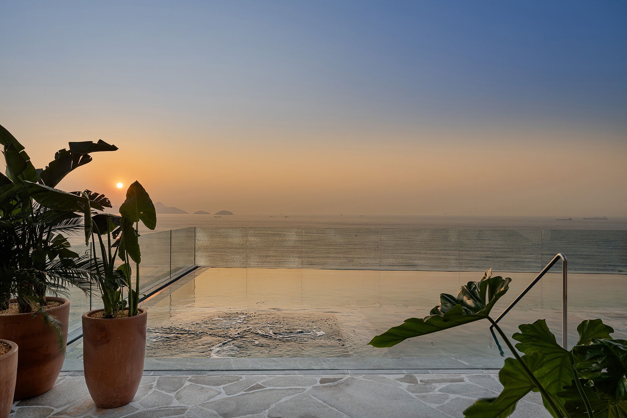 A sunset view from a balcony with potted plants and a clear view of the ocean.