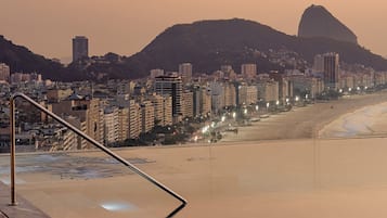 Paisagem costeira urbana com uma montanha imponente ao fundo, uma praia e uma escadaria que desce até a praia.