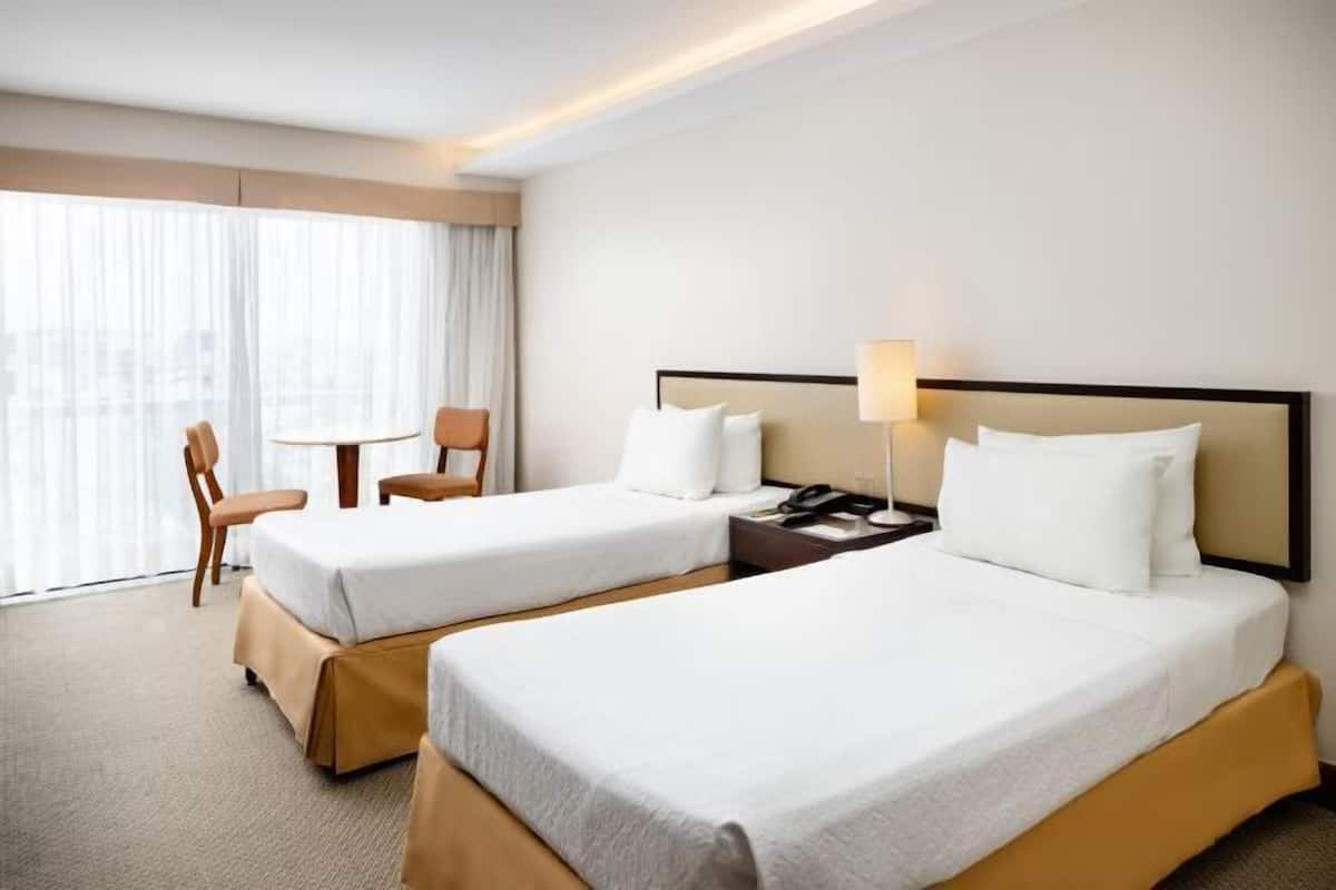 A hotel room with two beds, a desk, a chair, and a window with curtains.