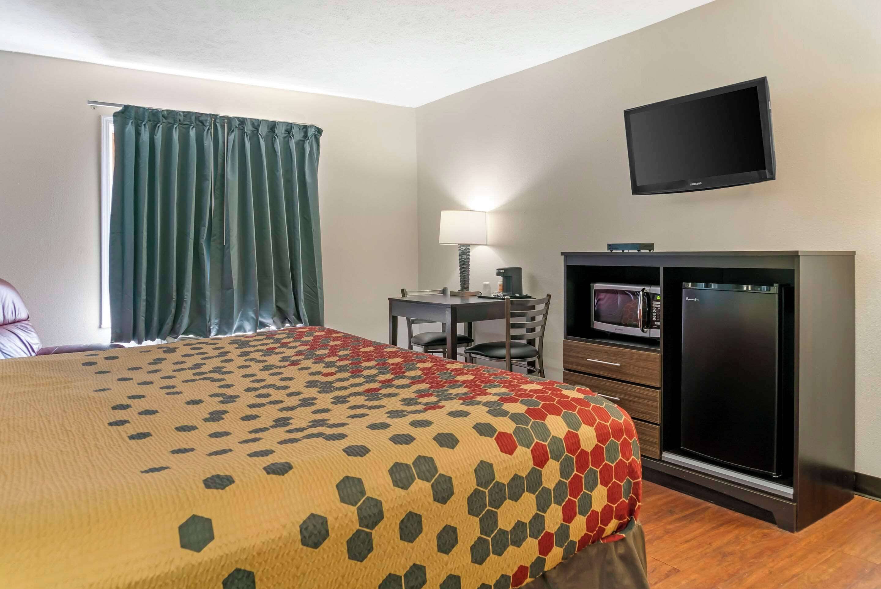 A hotel room with a bed, a desk, a television, a microwave, and a refrigerator.
