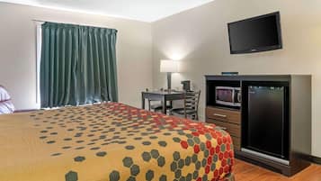 A hotel room with a bed, a desk, a television, a microwave, and a refrigerator.