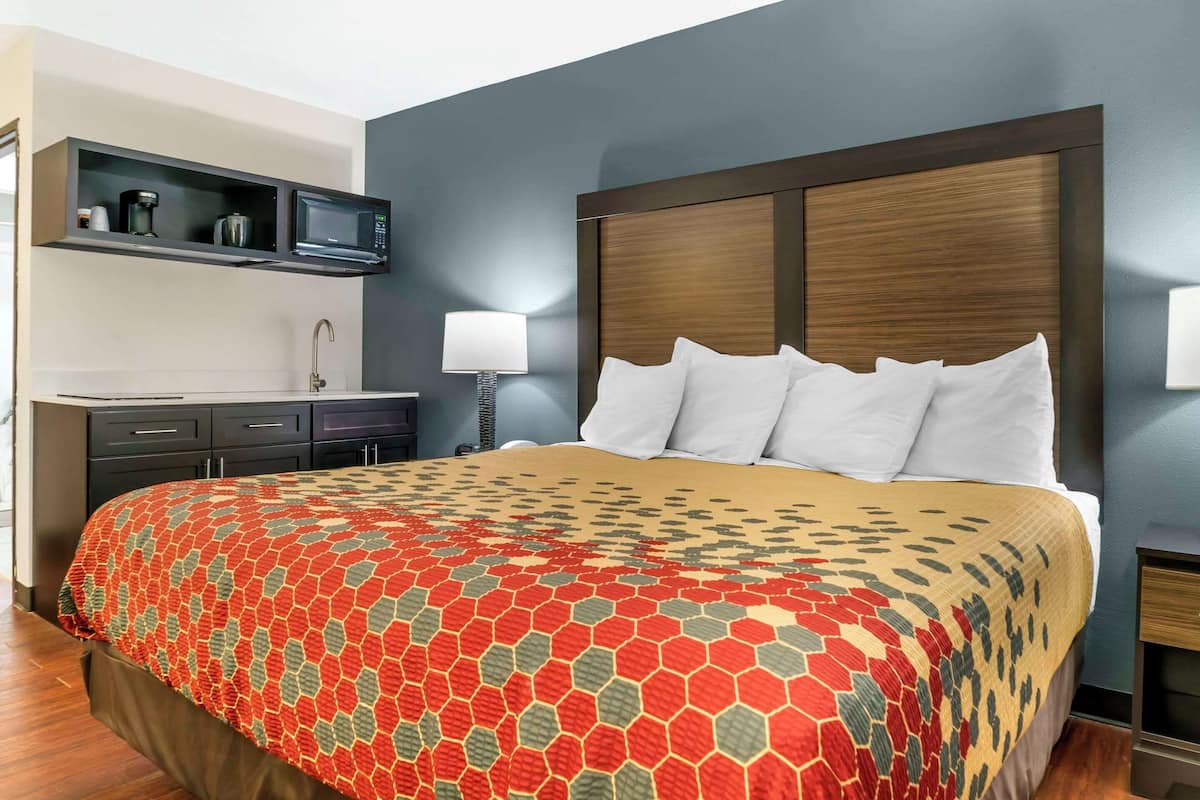 A hotel room with a large bed, a built-in TV, a coffee maker, and a small desk with drawers.