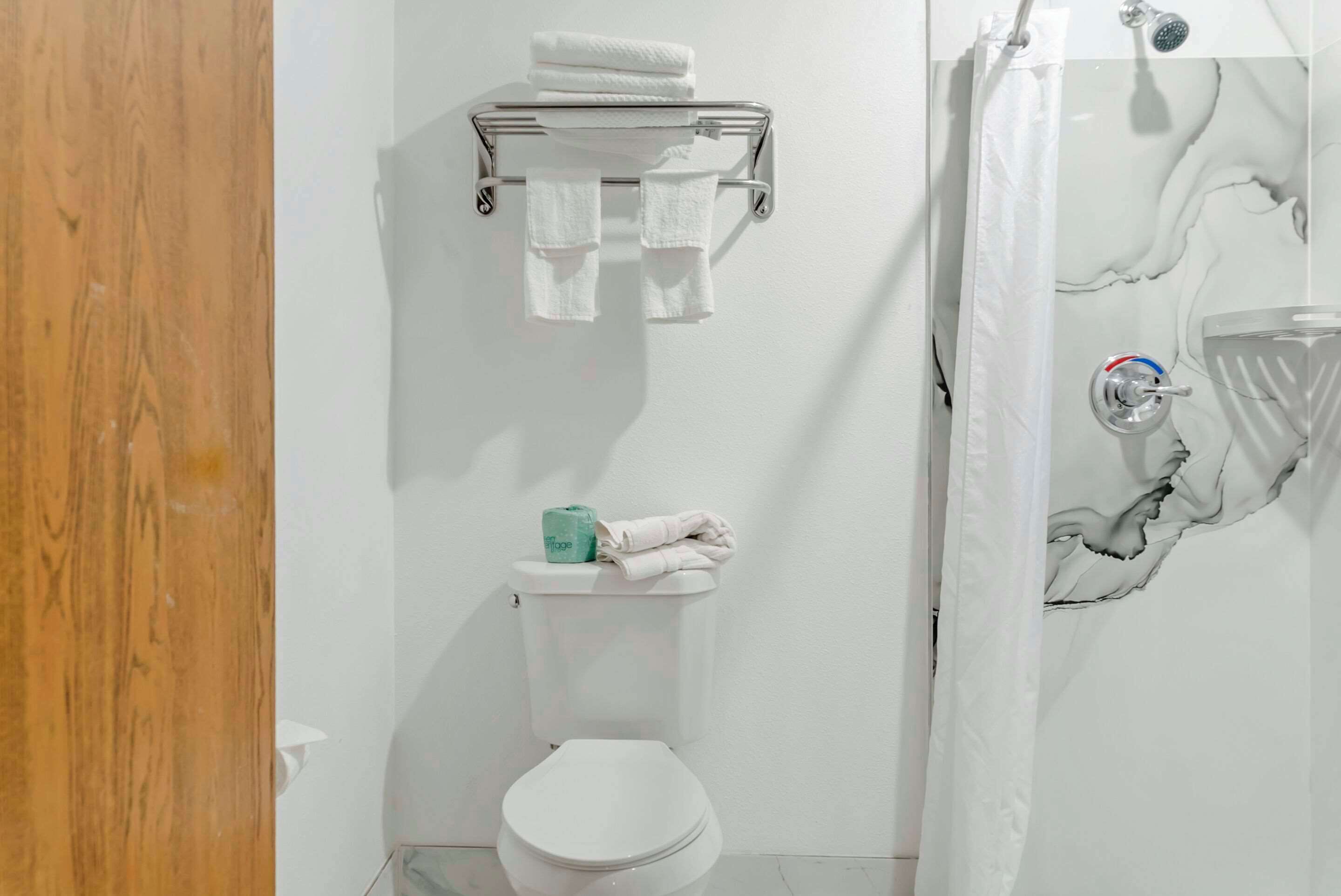 A bathroom with a toilet, a towel rack with towels, a shower curtain, and a toilet paper holder.