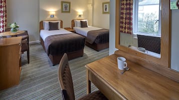Quarto de hotel com duas camas, uma secretária de madeira, uma cadeira, uma mesa com uma chávena e uma janela com cortinas.