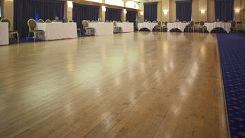 A conference room with multiple tables and chairs, wooden floors, and blue curtains.