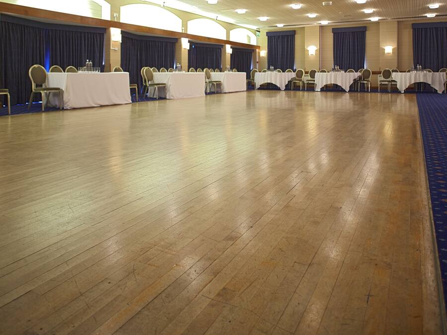 A conference room with multiple tables and chairs, wooden floors, and blue curtains.