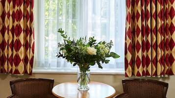 A room with a window, two chairs, and a table with a vase of flowers.
