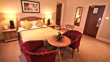 Quarto de hotel com uma cama, duas mesas de cabeceira, uma mesinha de apoio, uma mesa redonda de madeira com cadeiras e um espelho na parede.