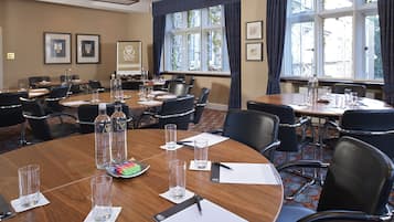 A conference room with multiple tables, chairs, and a large window with curtains.