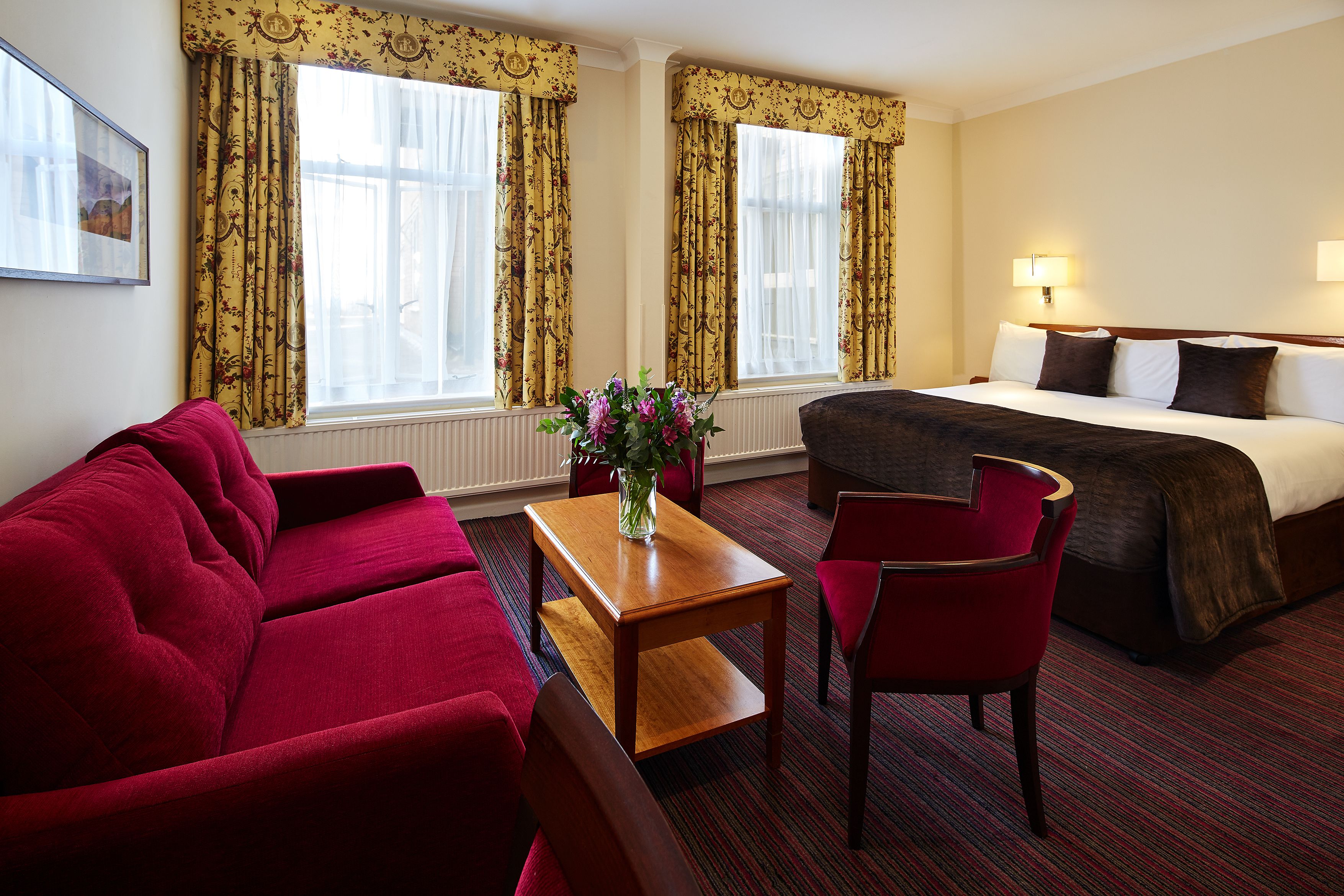 Quarto de hotel com uma cama, um sofá vermelho, uma mesa de madeira e uma cadeira.