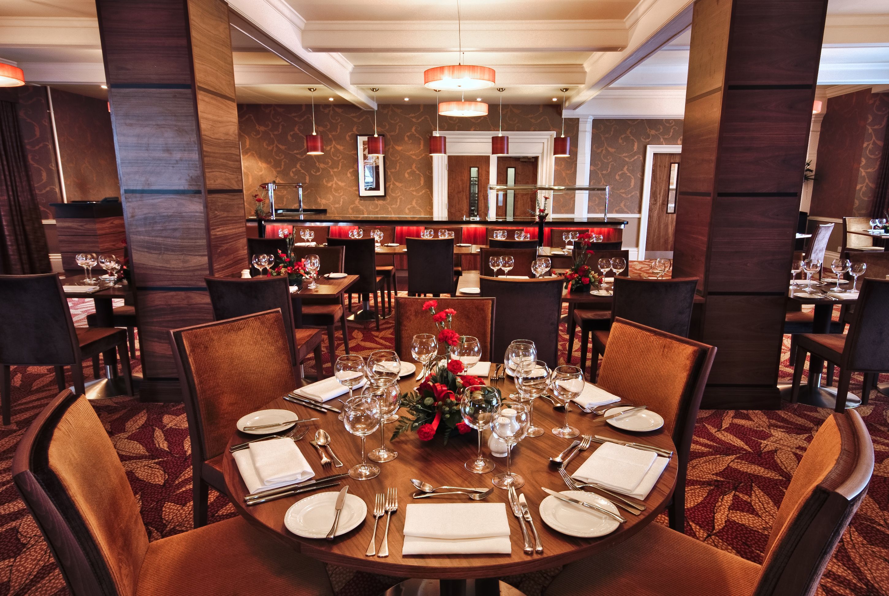 A formal dining area with round tables set for multiple guests, featuring a central floral arrangement and a mirror above the tables.