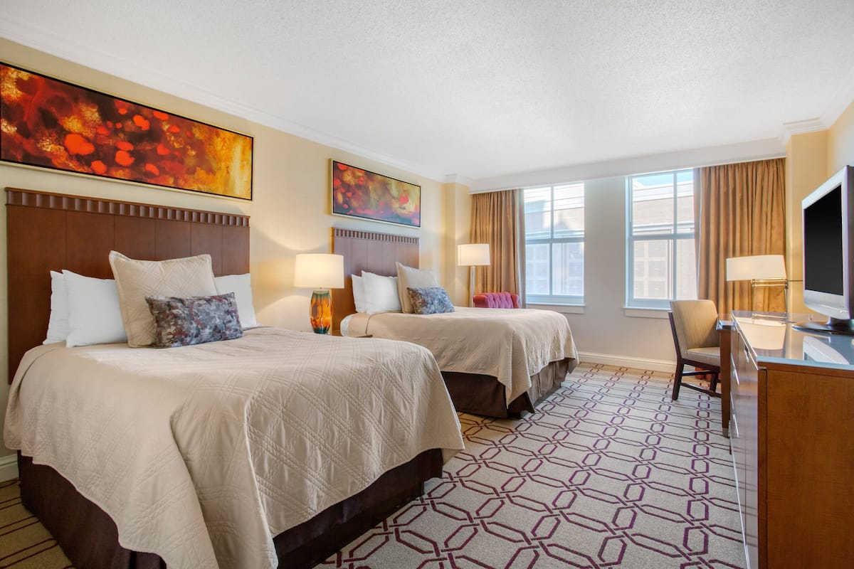 A hotel room with two beds, a desk, and a TV.