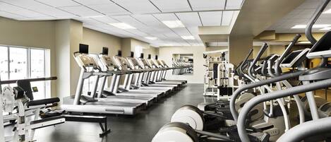 Un gimnasio con cintas de correr, máquinas de pesas y un espejo grande.
