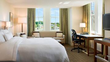 A hotel room with a large bed, a desk, a chair, and a TV.