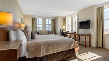 A hotel room with a large bed, a desk, a television, and a view of the city.