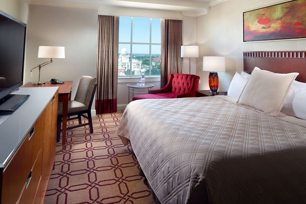 A hotel room with a large bed, a desk with a chair, a TV, and a window with curtains.