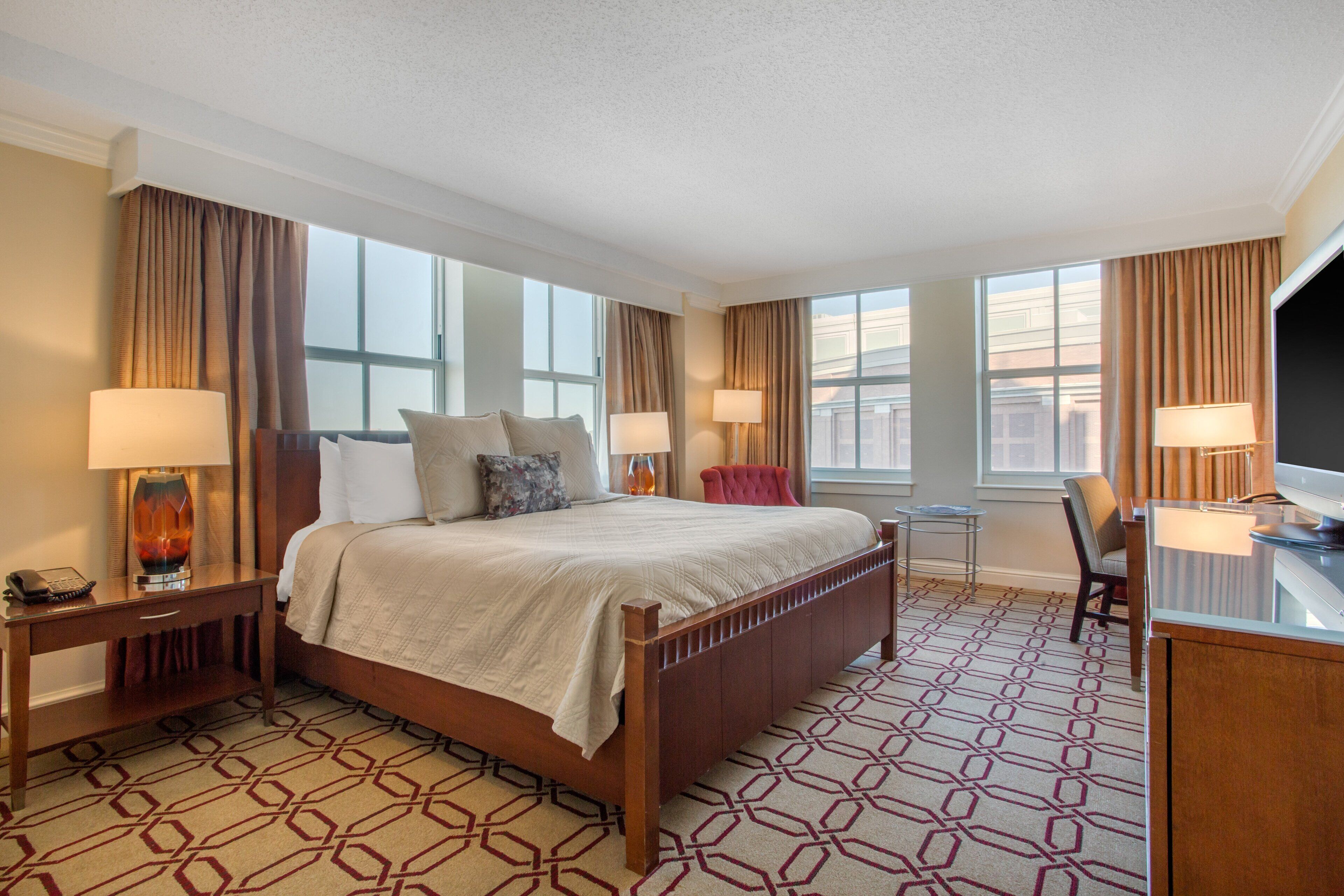A hotel room with a large bed, bedside lamps, a desk, and a chair.