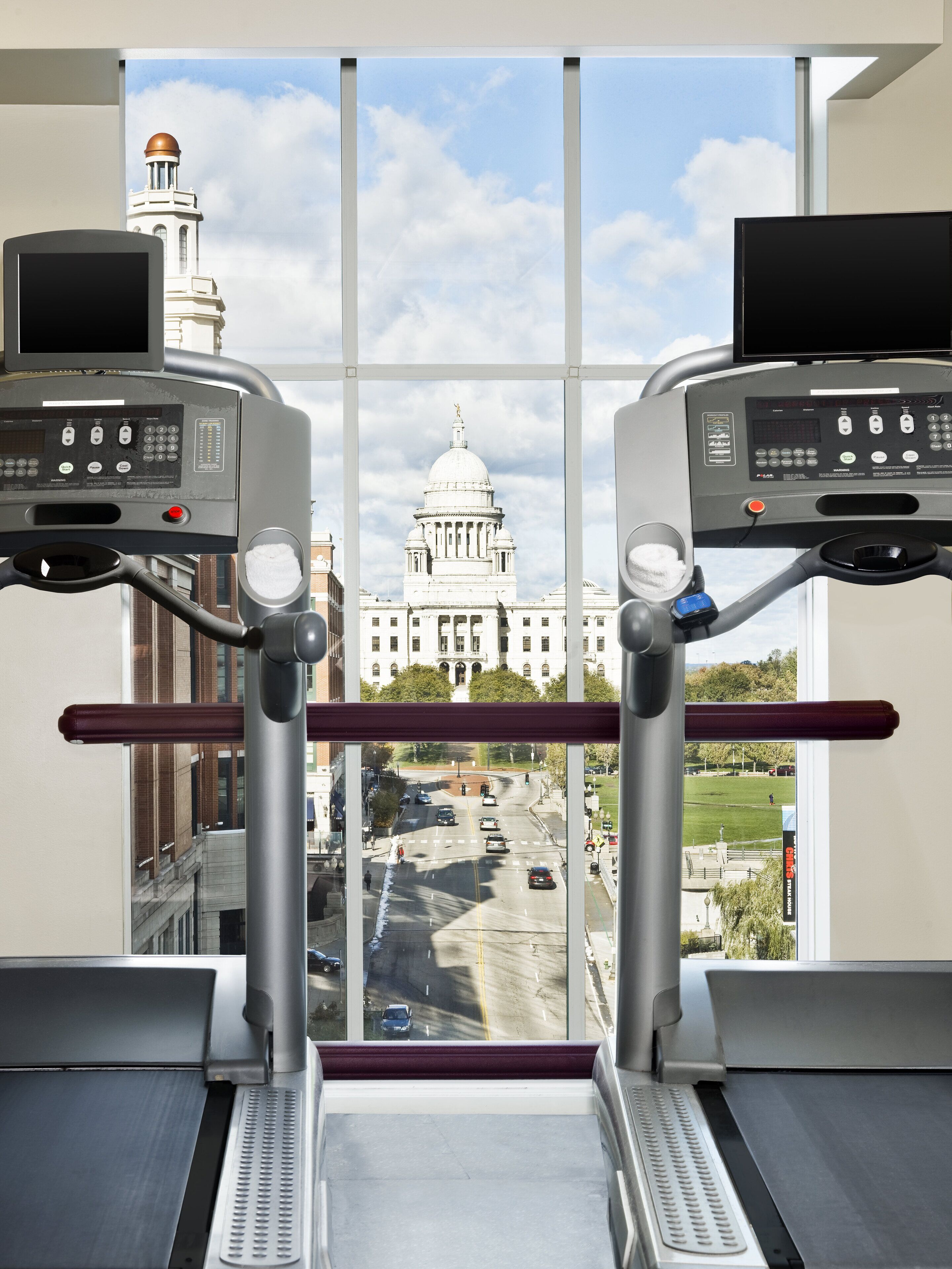 A treadmill with a view of a large building with a dome and a clock tower through a window.