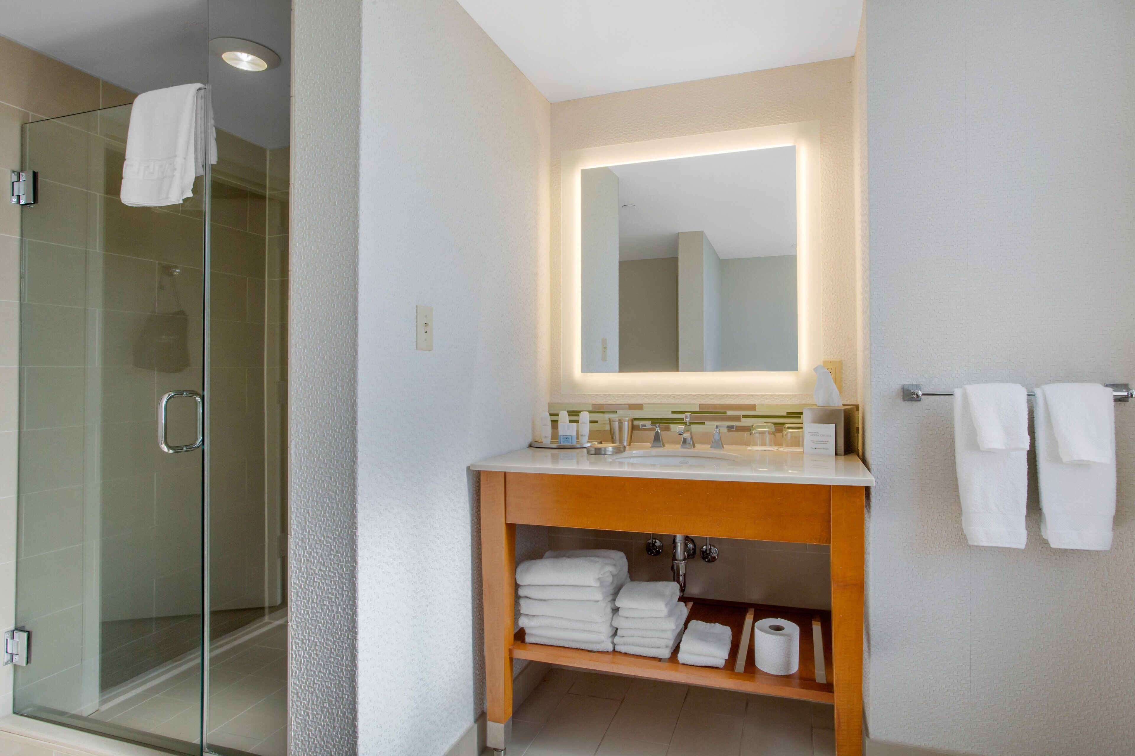 A modern bathroom with a glass shower enclosure, a wooden vanity with a mirror, and neatly folded towels.