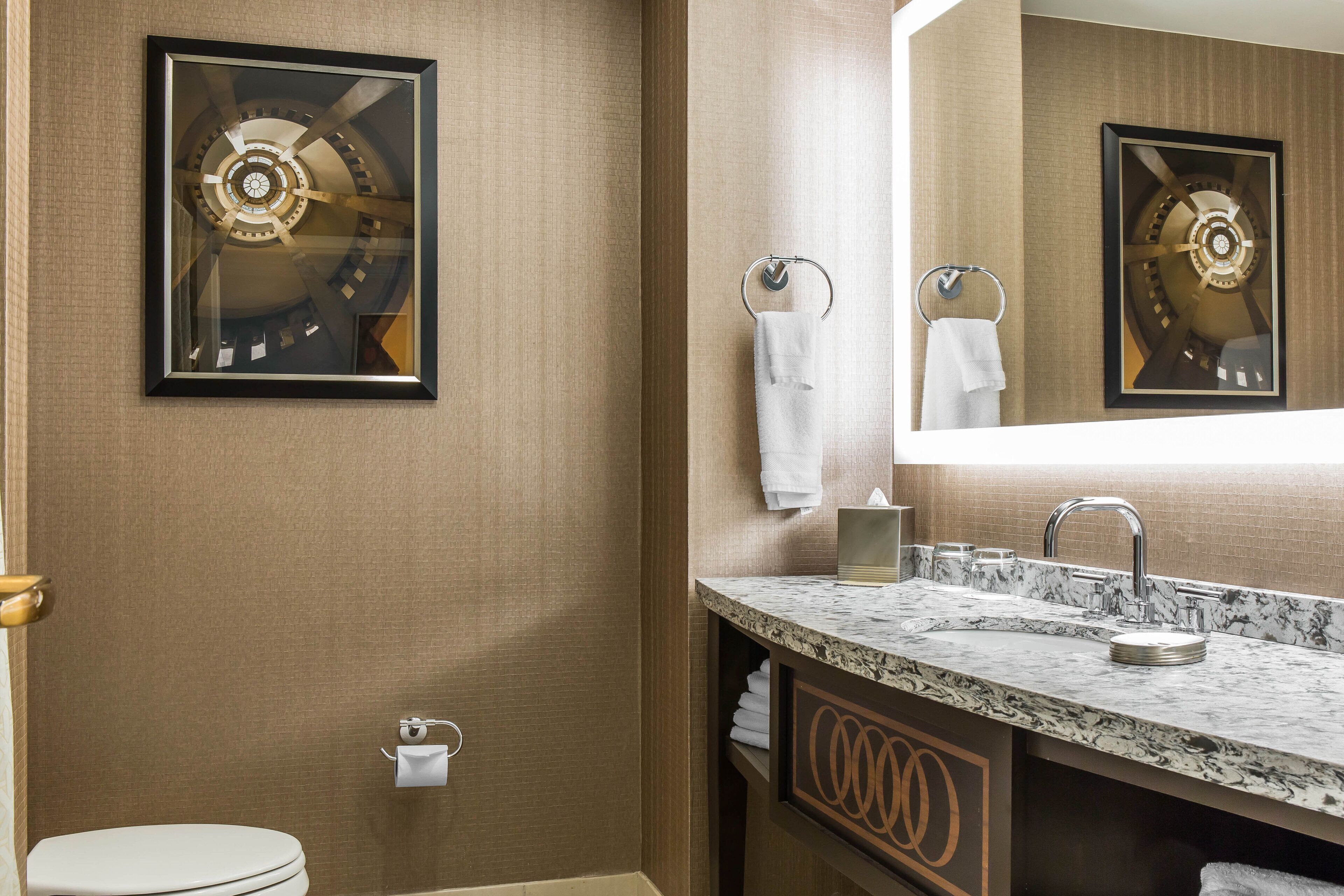 Une salle de bain avec un lavabo en marbre, des toilettes et une œuvre d’art encadrée au mur.