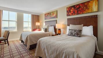 A hotel room with two beds, a chair, and large windows.
