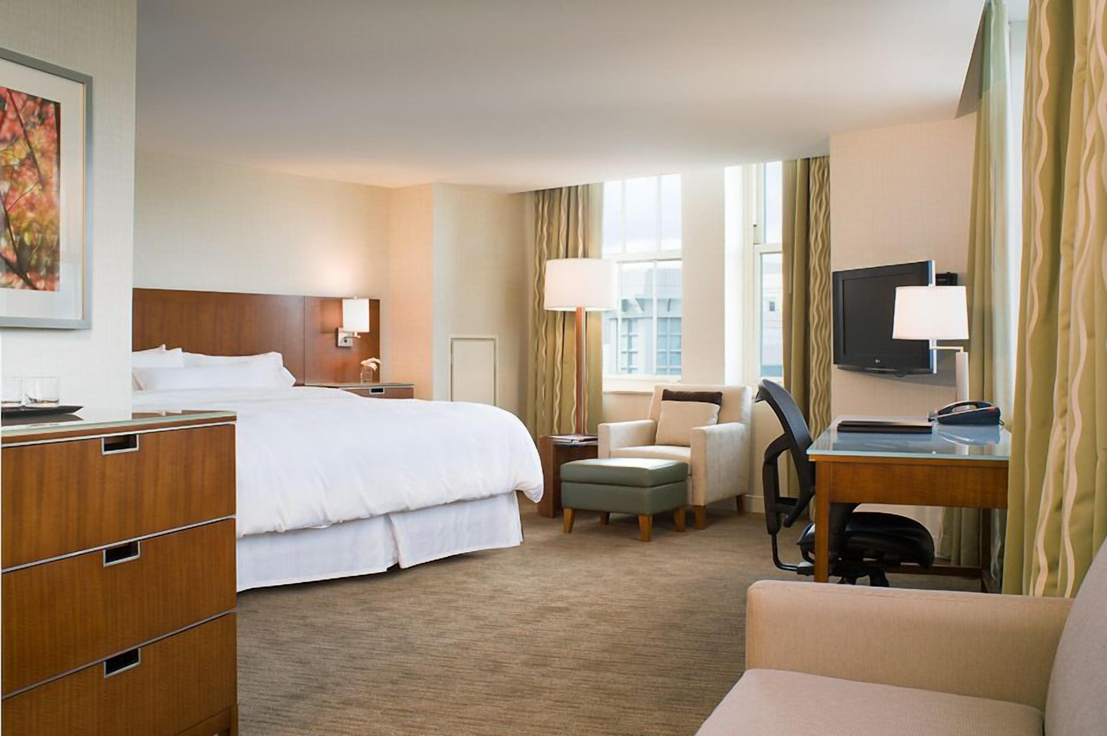 A hotel room with a bed, desk, chair, and a television.