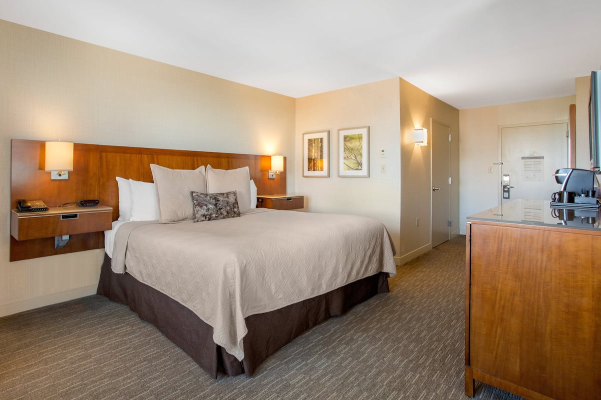 A hotel room with a large bed, bedside lamps, a wooden headboard, a desk with a telephone, and a dresser.