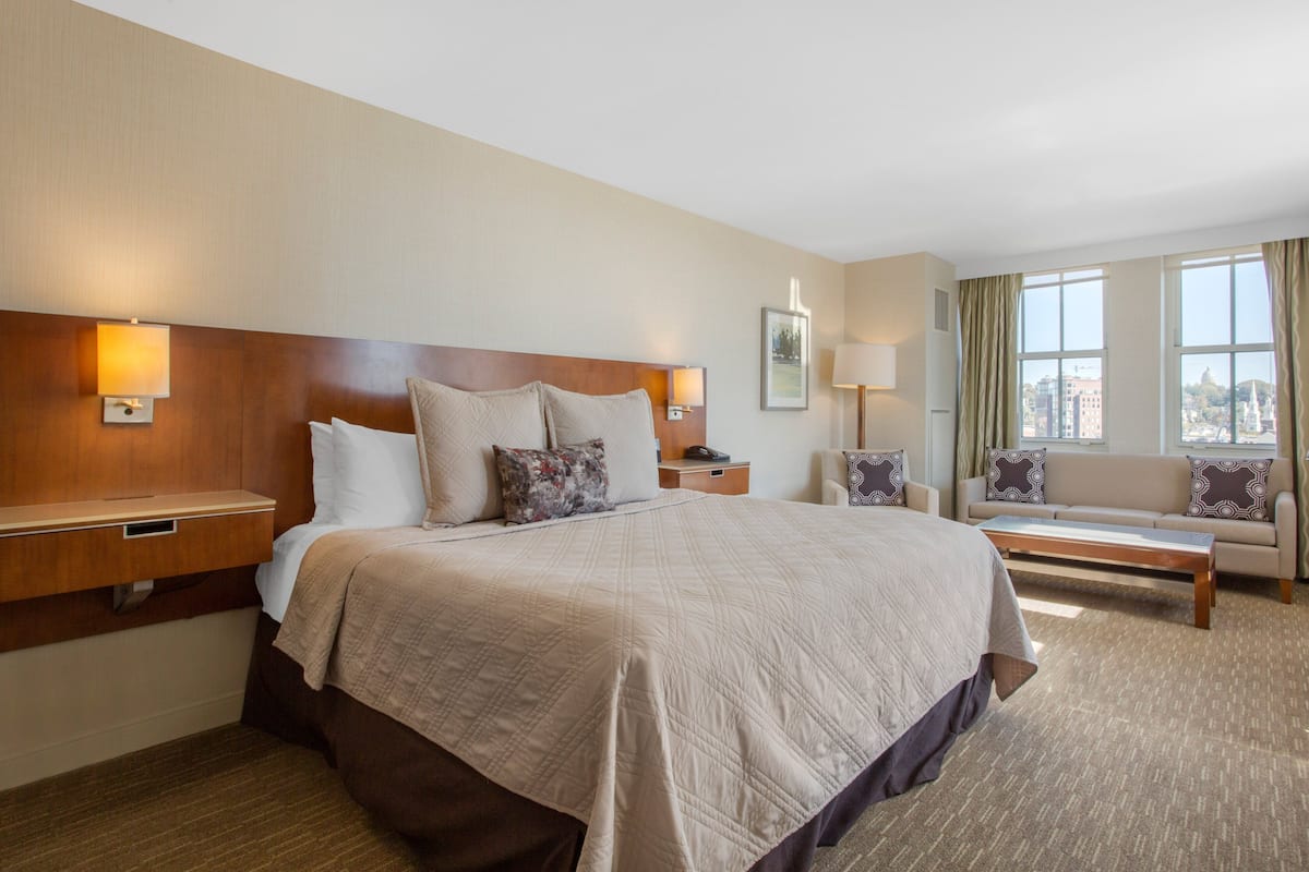 A hotel room with a large bed, a sofa, a nightstand, and a lamp.