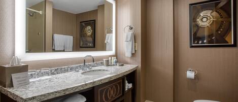 A modern bathroom with a large mirror, dual sinks, a toilet, and a framed artwork on the wall.