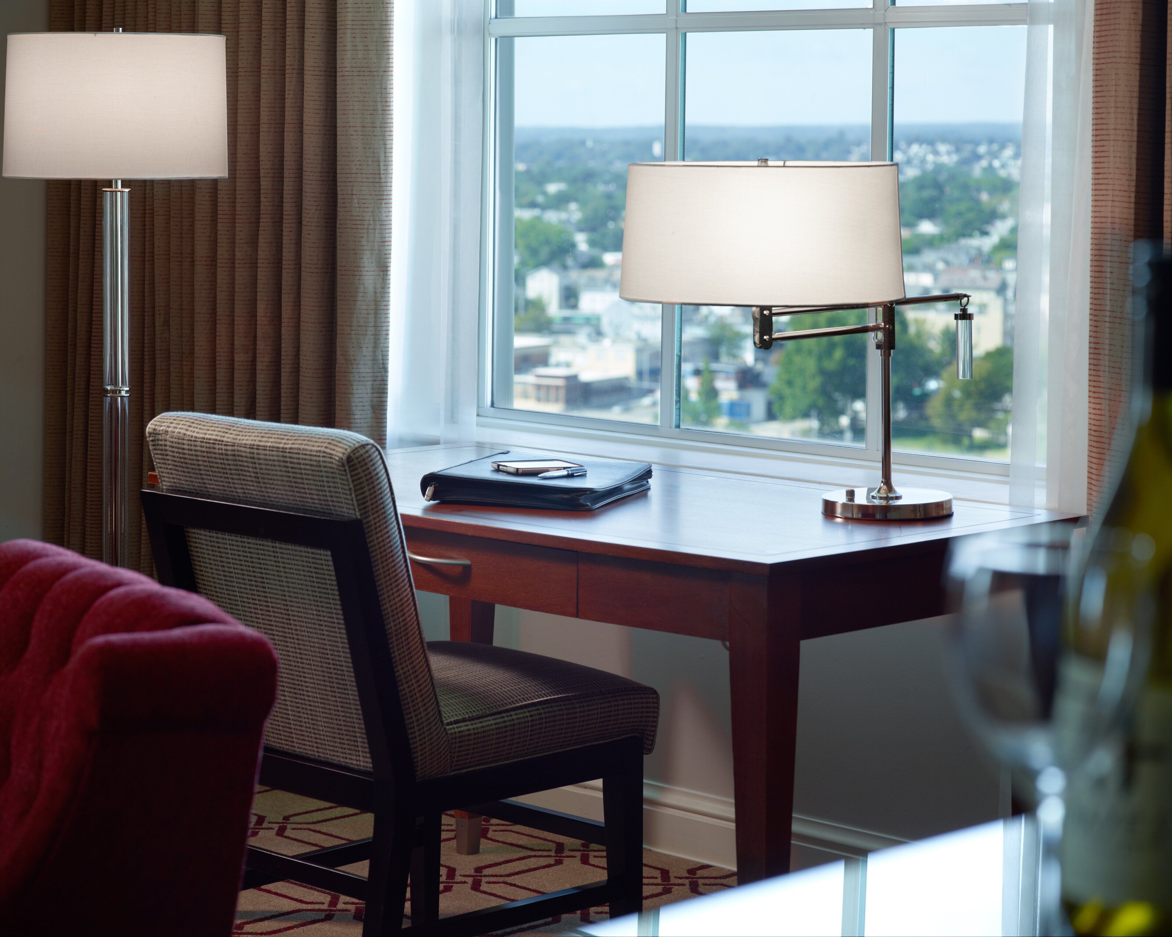 A hotel room with a desk, two lamps, a chair, and a view of the city.