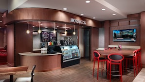 Interior de una cafetería con mostrador, zona de estar y una pantalla de televisión.