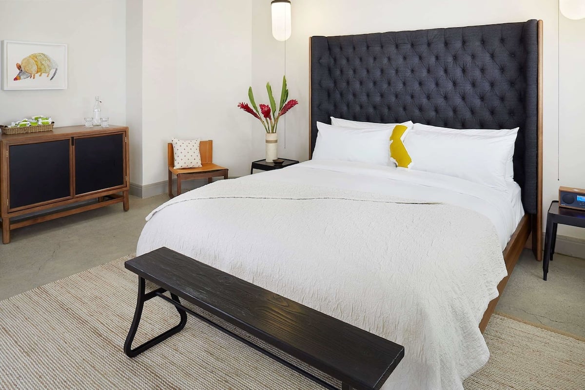 A neatly arranged bedroom with a large bed, a bedside table, a small cabinet, and a bench.